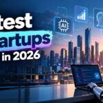 Hottest AI startups to watch in 2026 featured image showing a humanoid robot coding on a laptop in front of a city skyline, with floating icons for AI chips, robotics, cloud and security